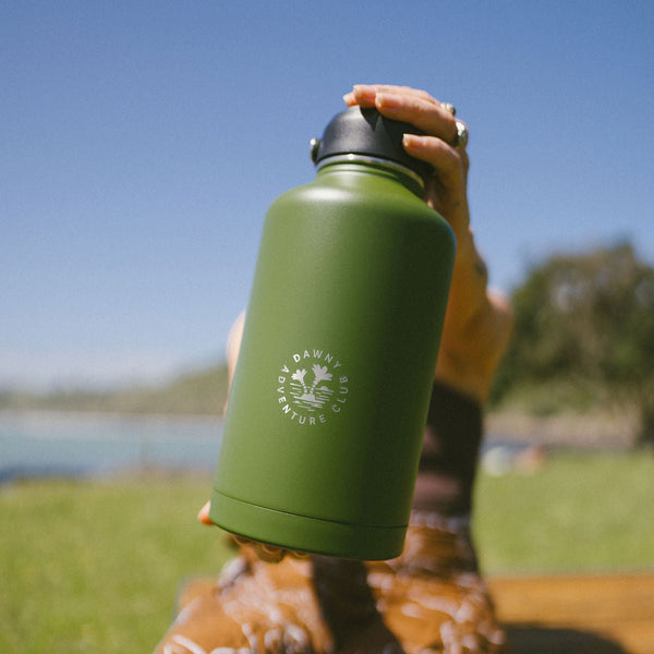 Person holding a green water bottle with a logo outdoors