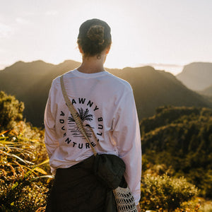 Person wearing a white sweatshirt with text and graphics, standing on a mountain with scenic view.