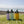 Three colorful water bottles with black lids on a grassy field with a clear sky.