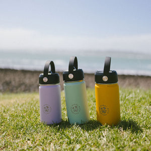 Three colorful water bottles with black lids on a grassy field with a clear sky.